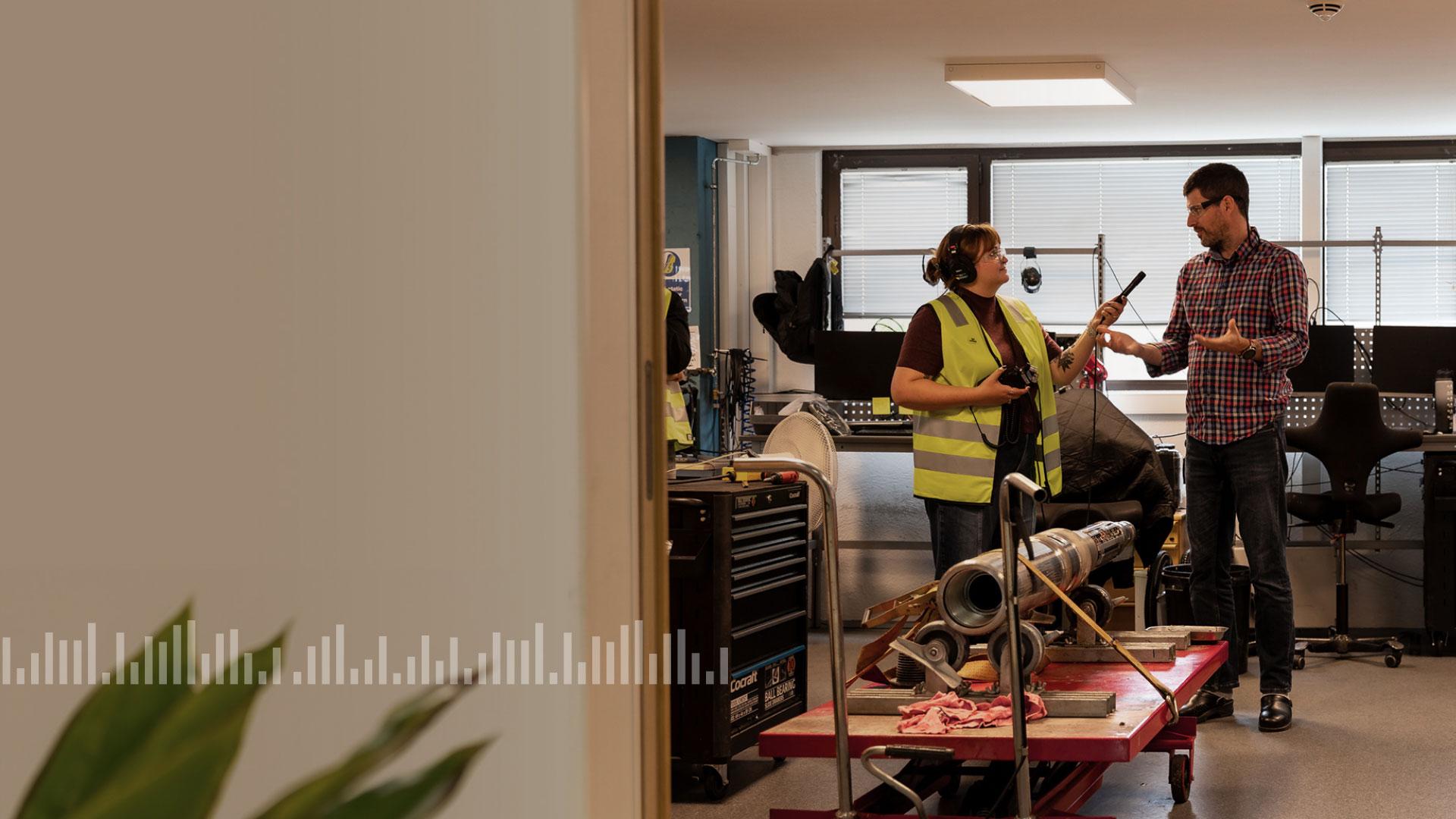 Audio interview taking place in a room with a wired drill pipe in view; includes a soundwave overlay