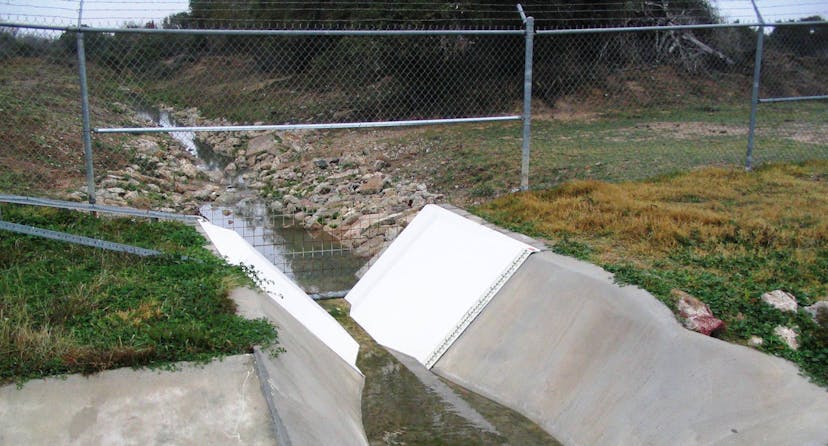 Trapzoidal flume installed in a creek, with a wire-link fence intersecting the creek